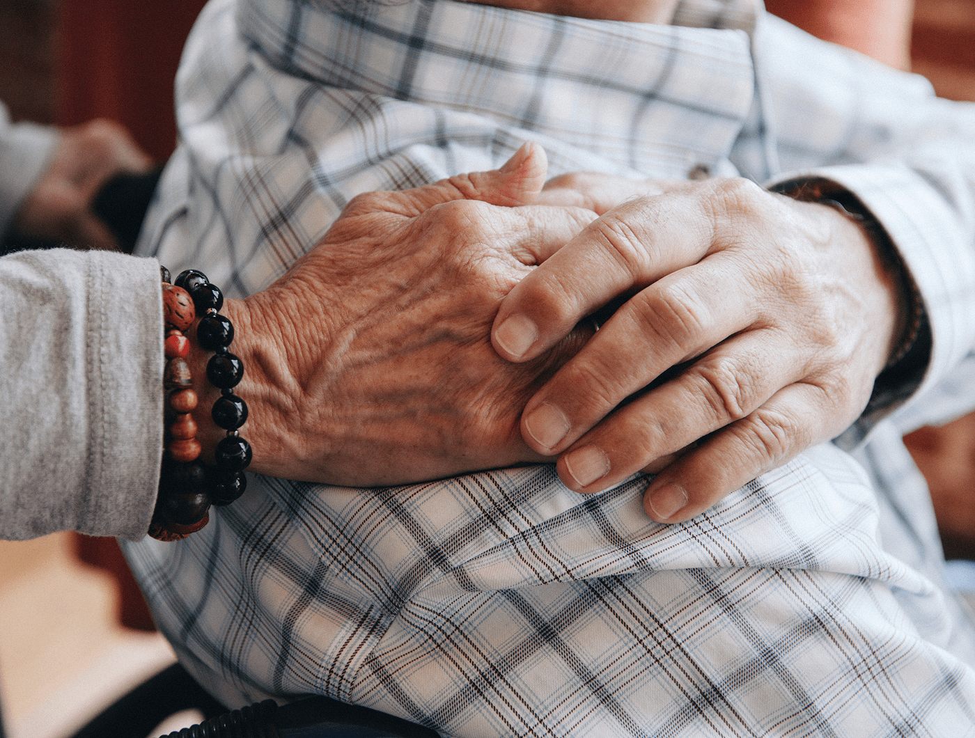 A care worker wearing a beaded bracelet holding an older adult's hands